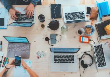 People sitting around a table top with different electronic, hearing and writing tools on it. 