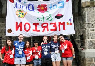 Customs People standing outside of Merion Hall with a banner behind them