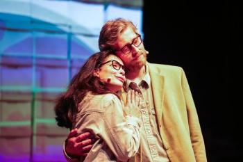 Two actors embrace in front of colorful screen